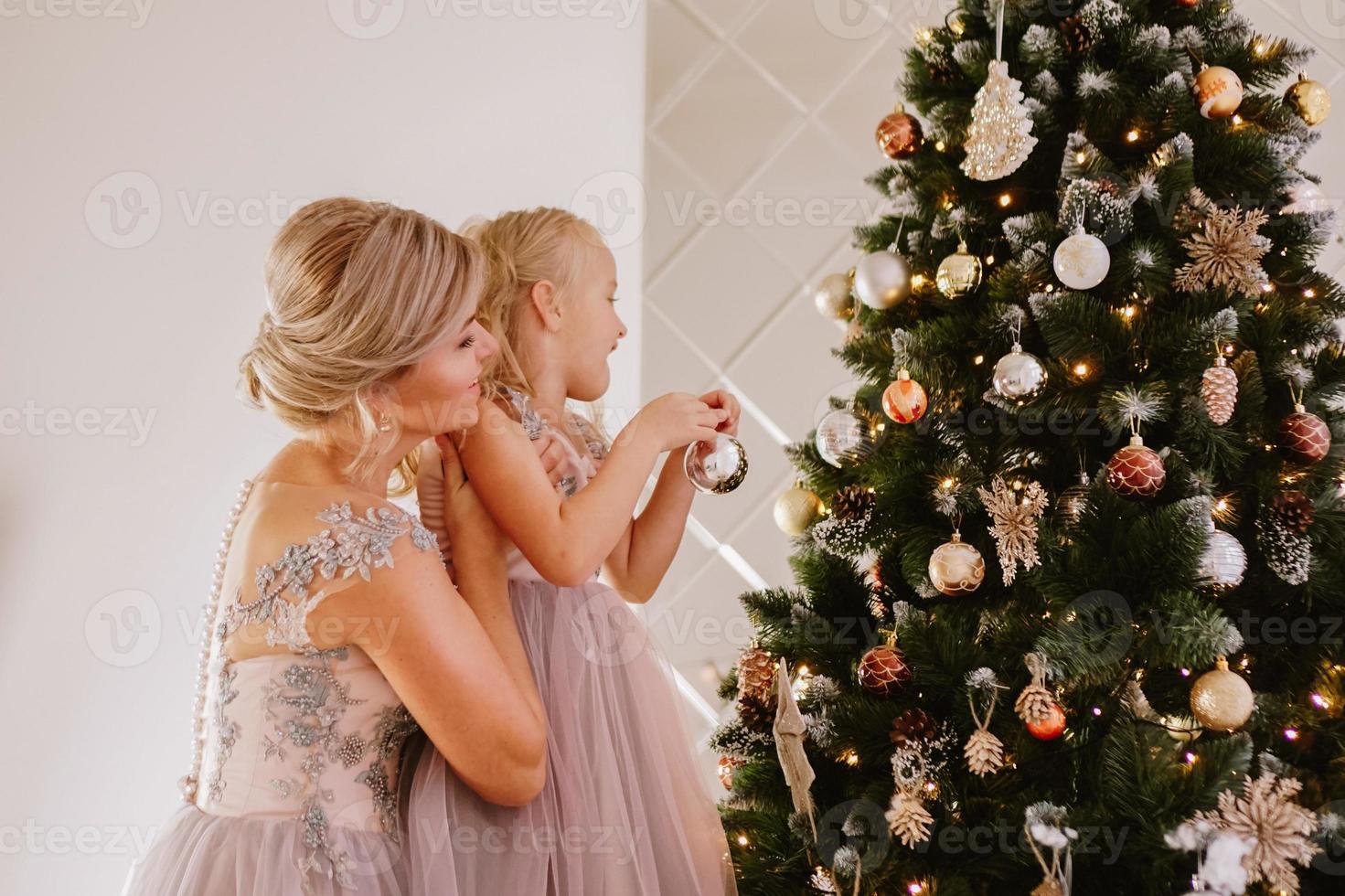 la giovane bella madre tiene la figlia che decora un albero di natale foto