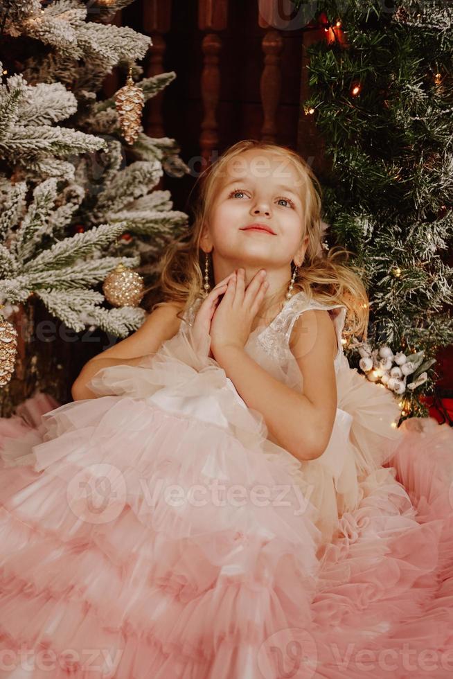 ragazza con un vestito rosa vicino all'albero di natale foto