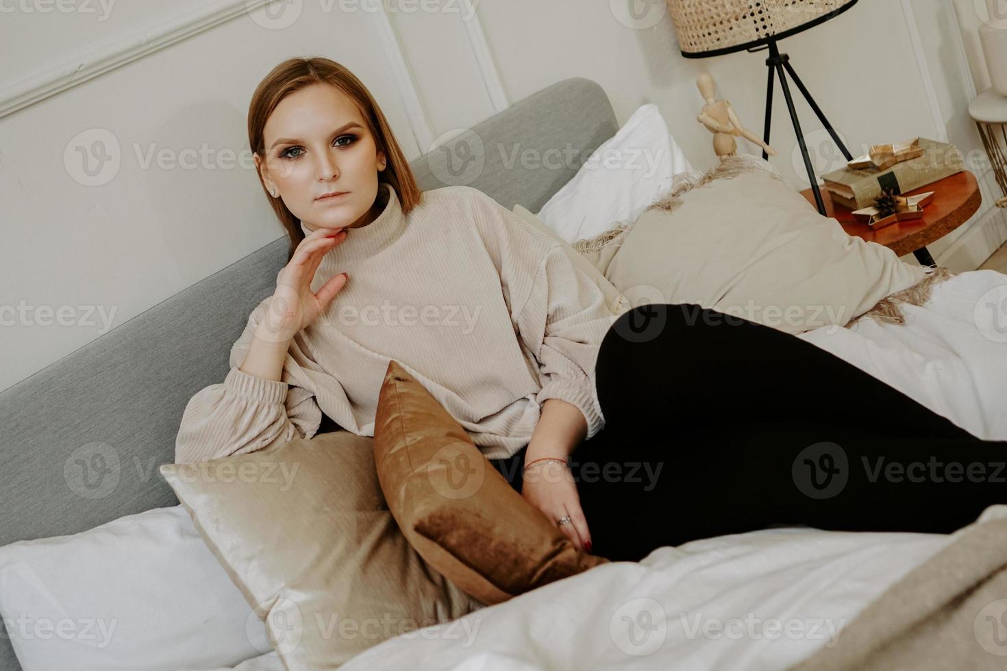 donna vestita con un maglione beige seduta sul letto foto