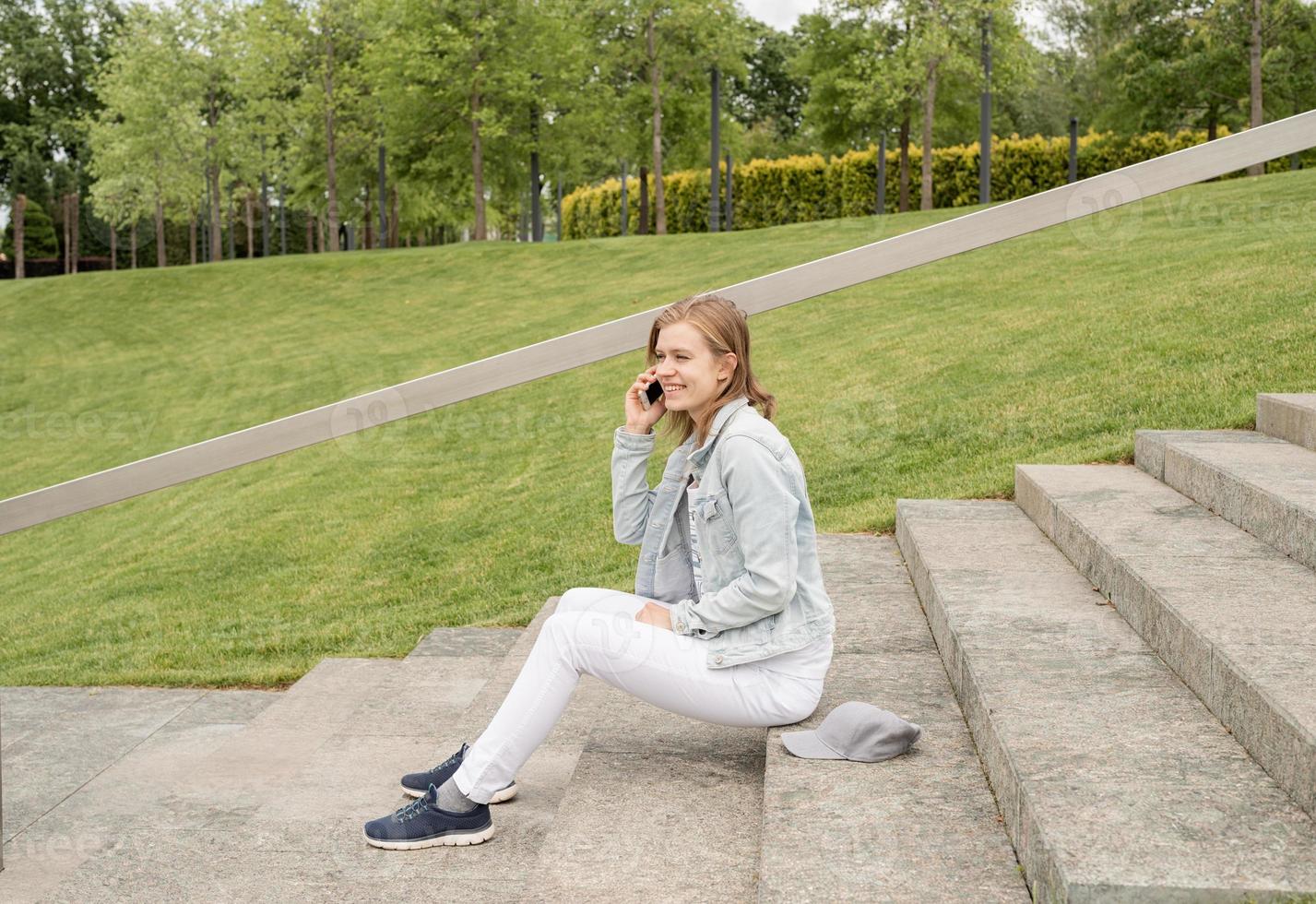 donna che scrive sul suo cellulare, seduta sulle scale nel parco foto