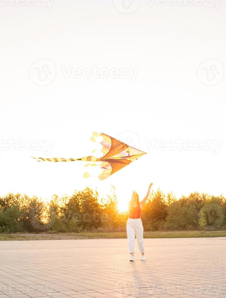 giovane donna che fa volare un aquilone in un parco pubblico al tramonto foto