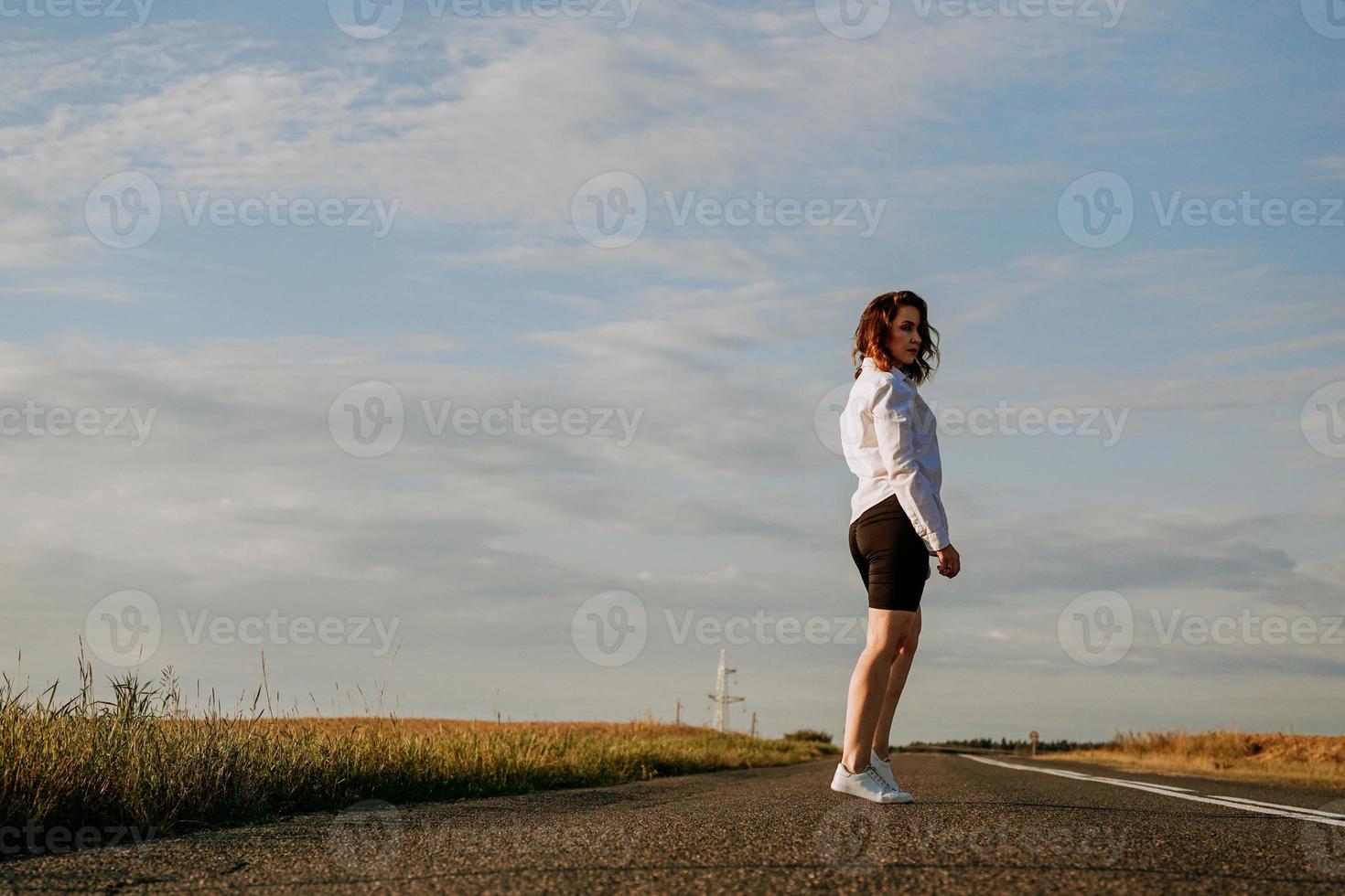 donna in camicia bianca cammina lungo la strada tra i campi foto