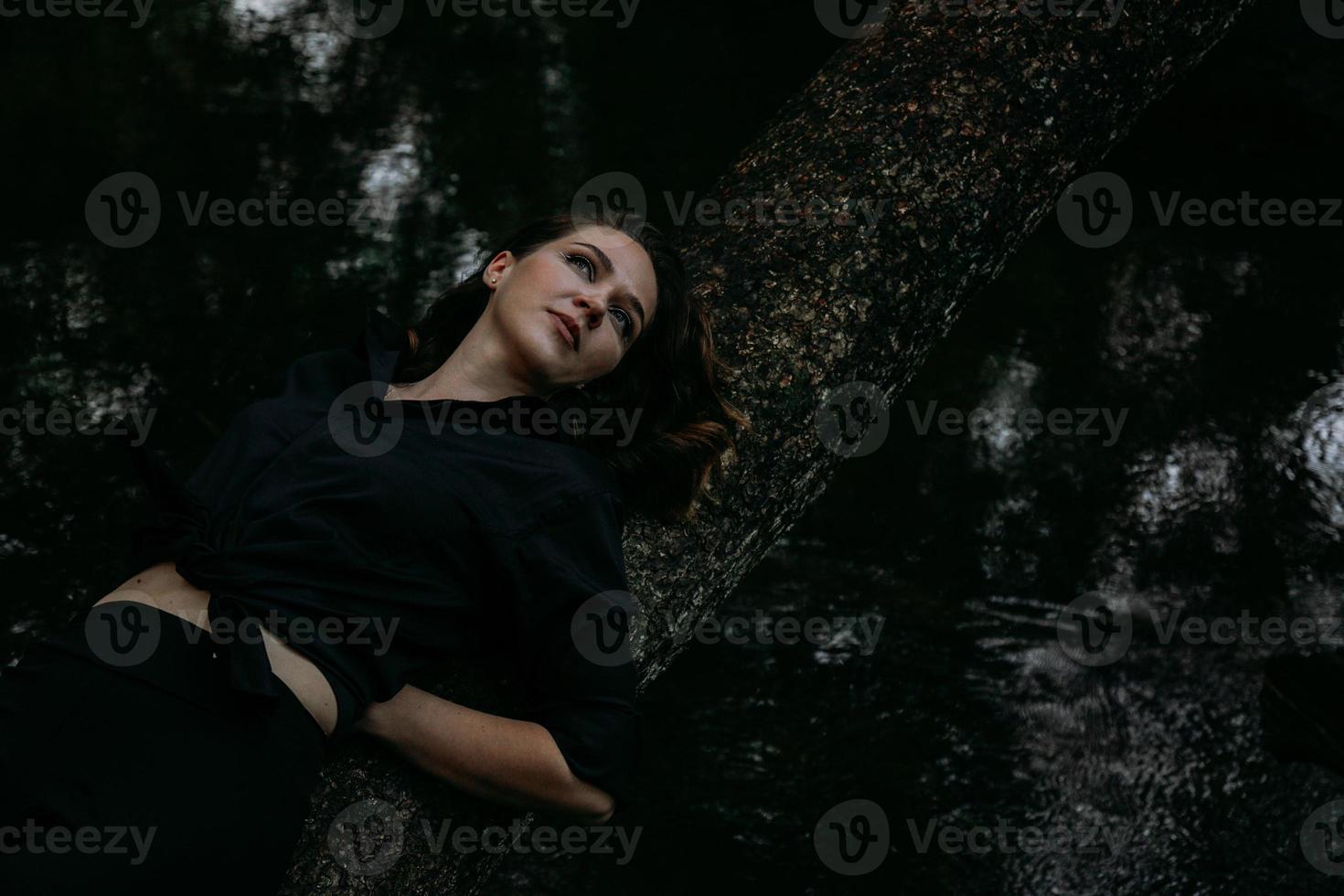 donna in abiti neri su uno sfondo d'acqua, giace su un albero foto