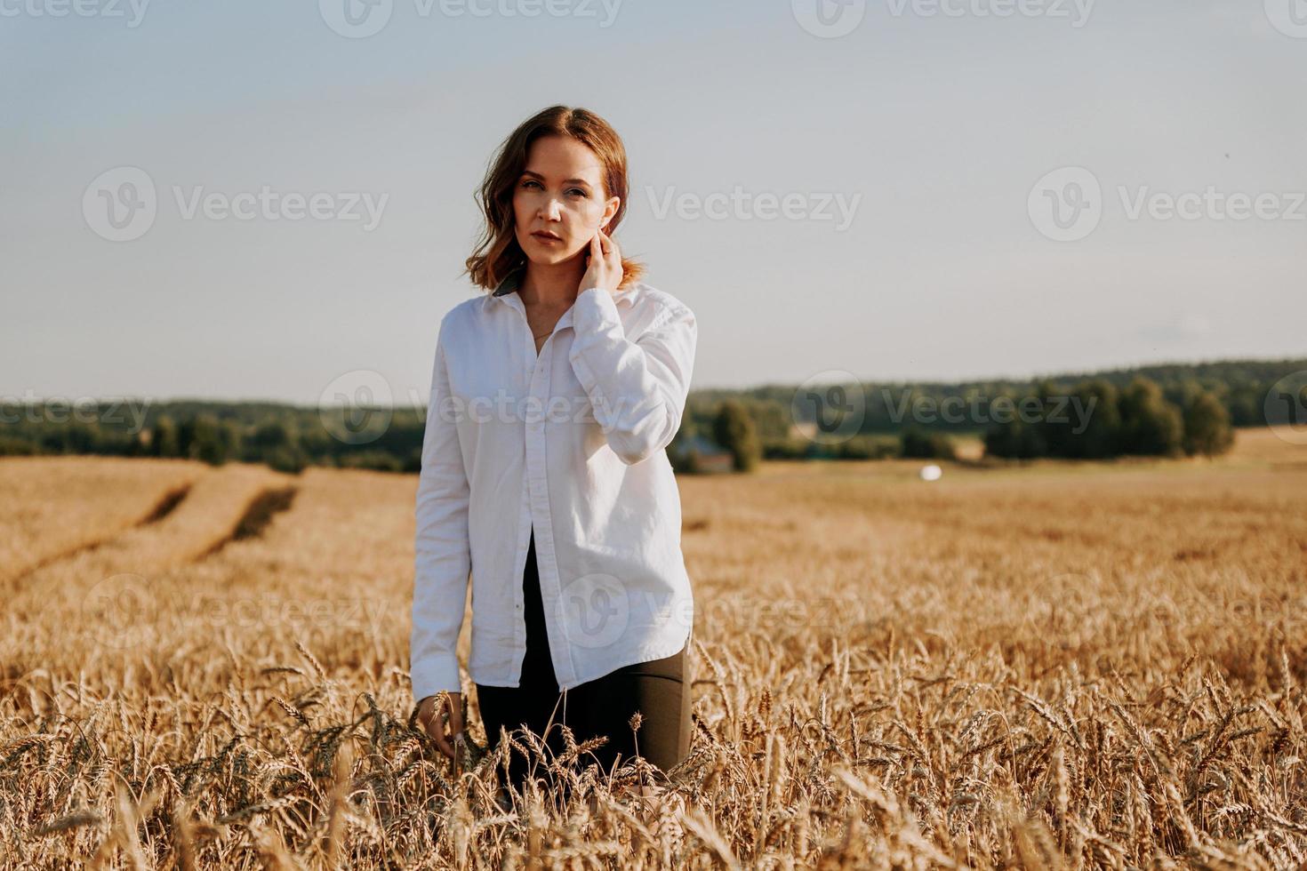 ragazza dai capelli rossi in una camicia bianca. lei in un campo di segale in una giornata di sole foto