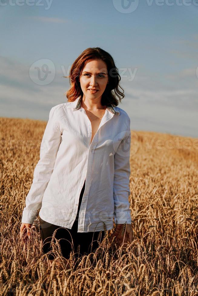 felice giovane donna in una camicia bianca in un campo di grano. giorno soleggiato. foto