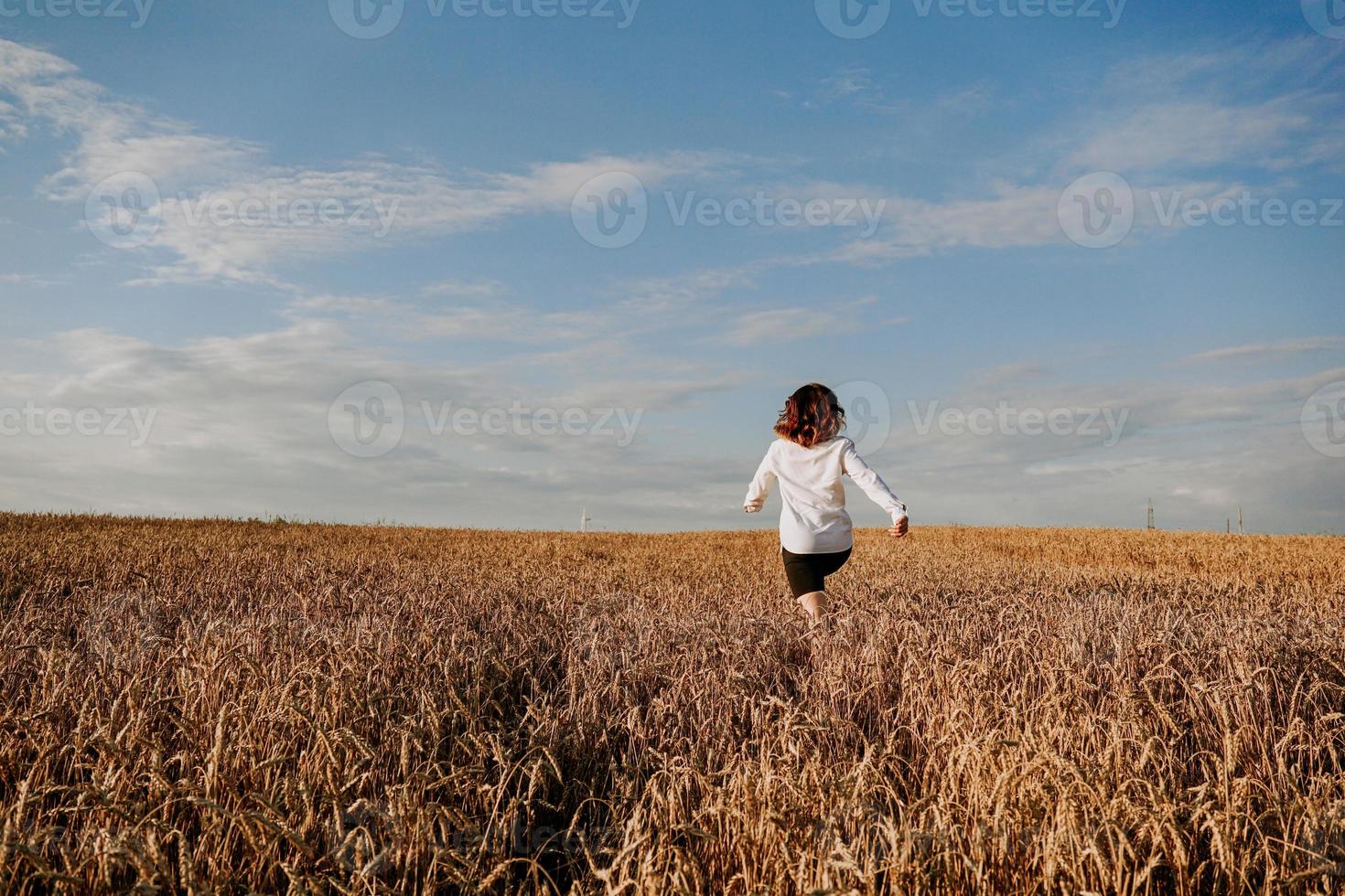 la donna corre in un campo di grano in una giornata estiva. concetto di felicità e gioia foto