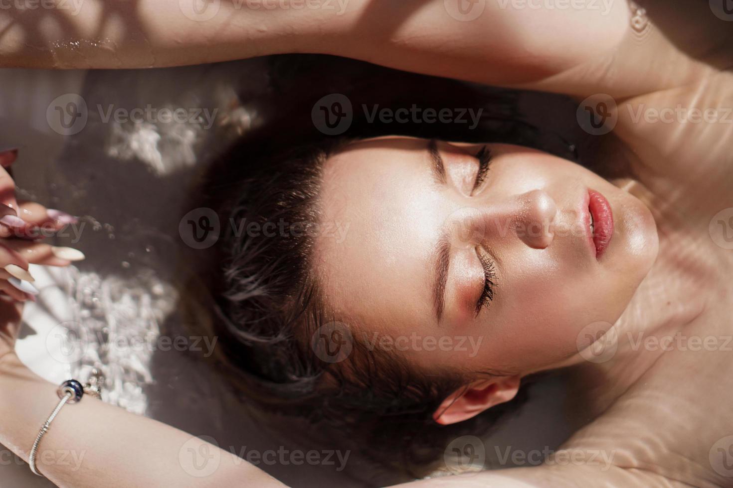 una ragazza attraente che si rilassa nella vasca da bagno su sfondo chiaro foto