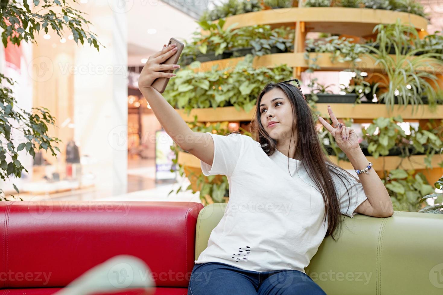 donna seduta sul divano nel centro commerciale, guardando il telefono foto