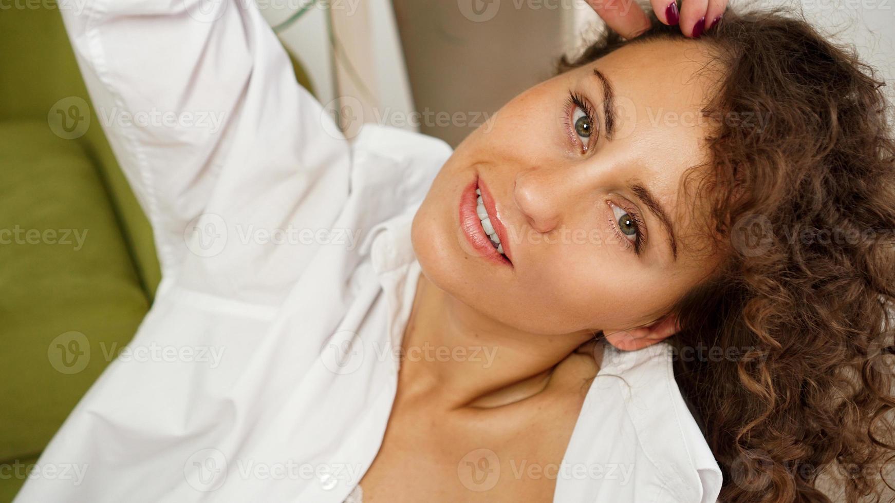 felice giovane donna con i capelli ricci in camicia bianca a casa foto