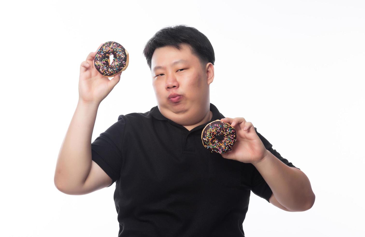 giovane uomo asiatico grasso divertente che gioca con le ciambelle al cioccolato foto