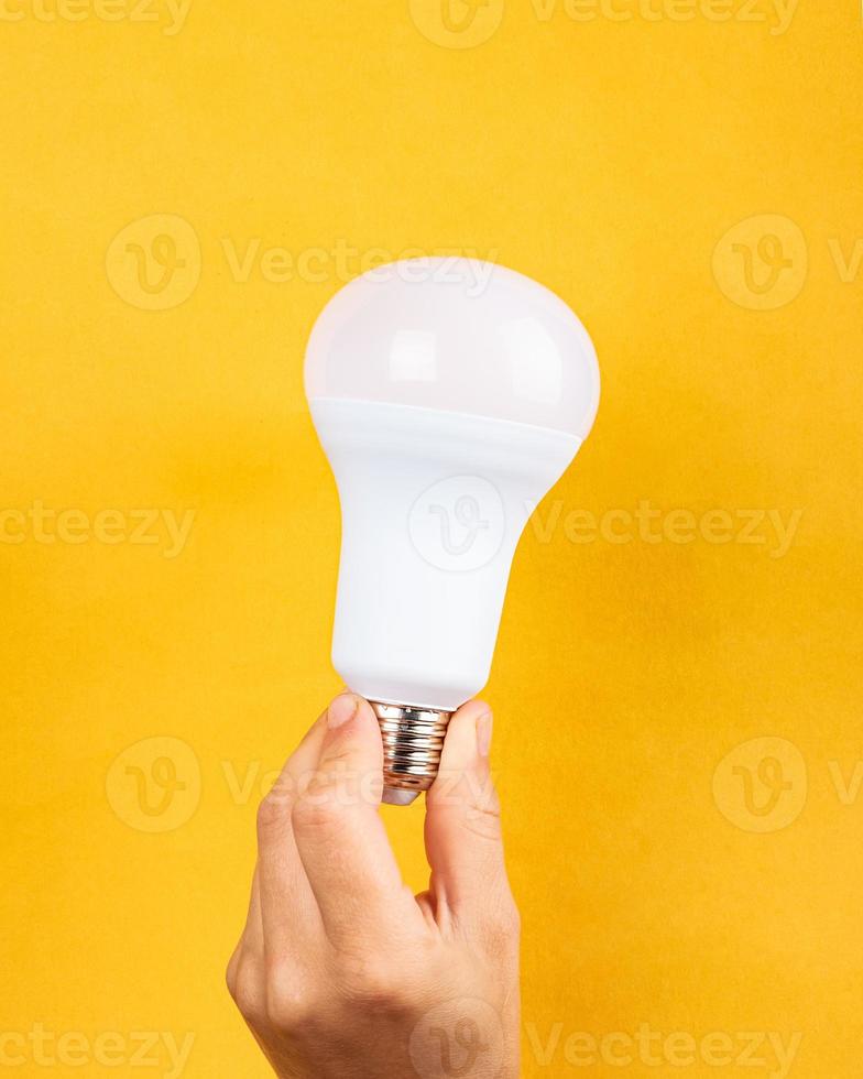 una lampadina in mano su sfondo giallo, concetto di aumento del prezzo dell'elettricità. foto