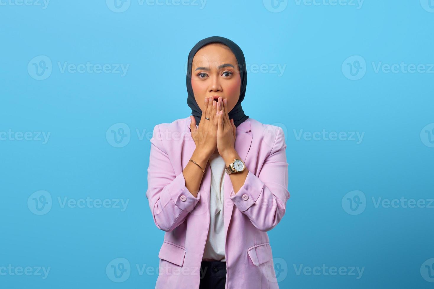 donna asiatica sorpresa che copre la bocca con le mani su sfondo blu foto
