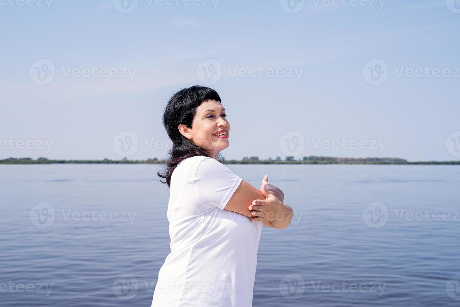 donna anziana attiva e felice che fa stretching vicino alla riva del fiume foto