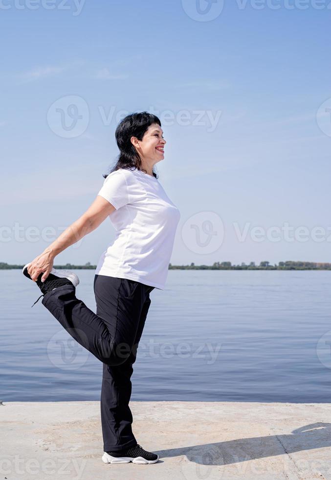 donna anziana attiva e felice che fa stretching vicino alla riva del fiume foto