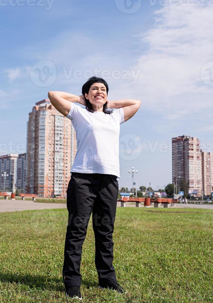 donna anziana sorridente che si scalda prima dell'allenamento all'aperto nel parco foto