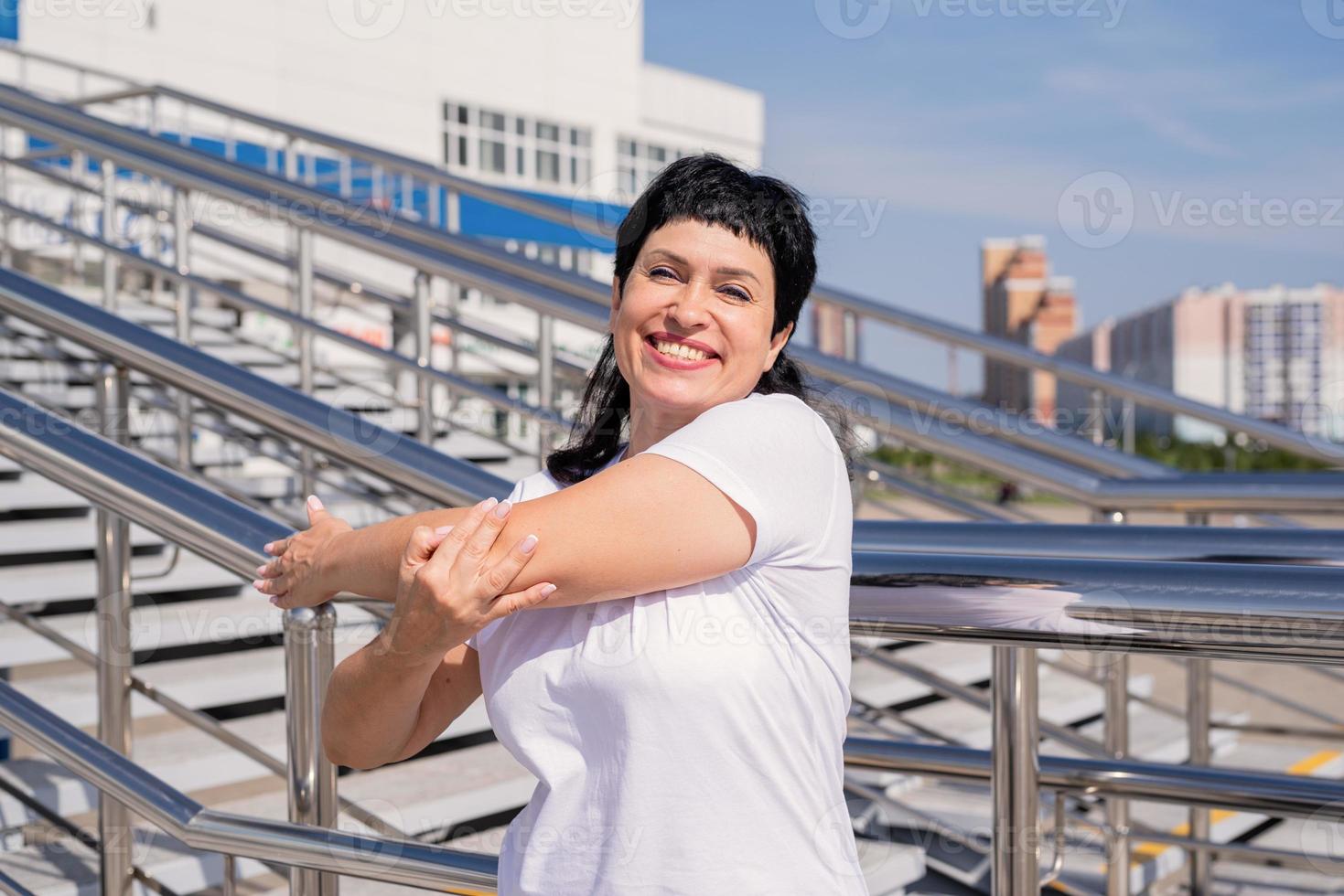 donna anziana sorridente che fa stretching all'aperto su sfondo urbano foto