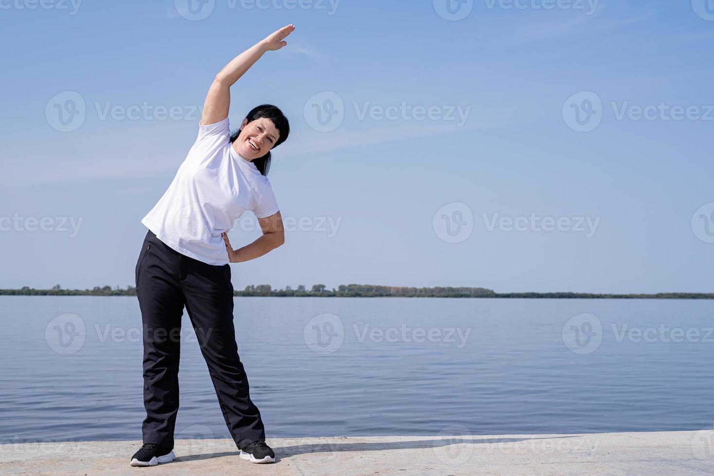 donna anziana attiva e felice che fa stretching vicino alla riva del fiume foto