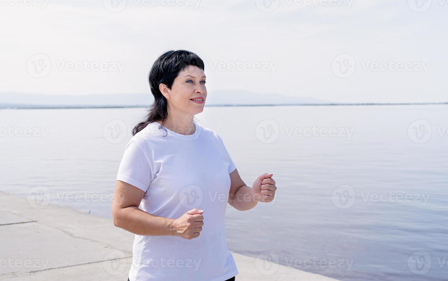 donna anziana attiva che fa jogging vicino alla riva del fiume foto