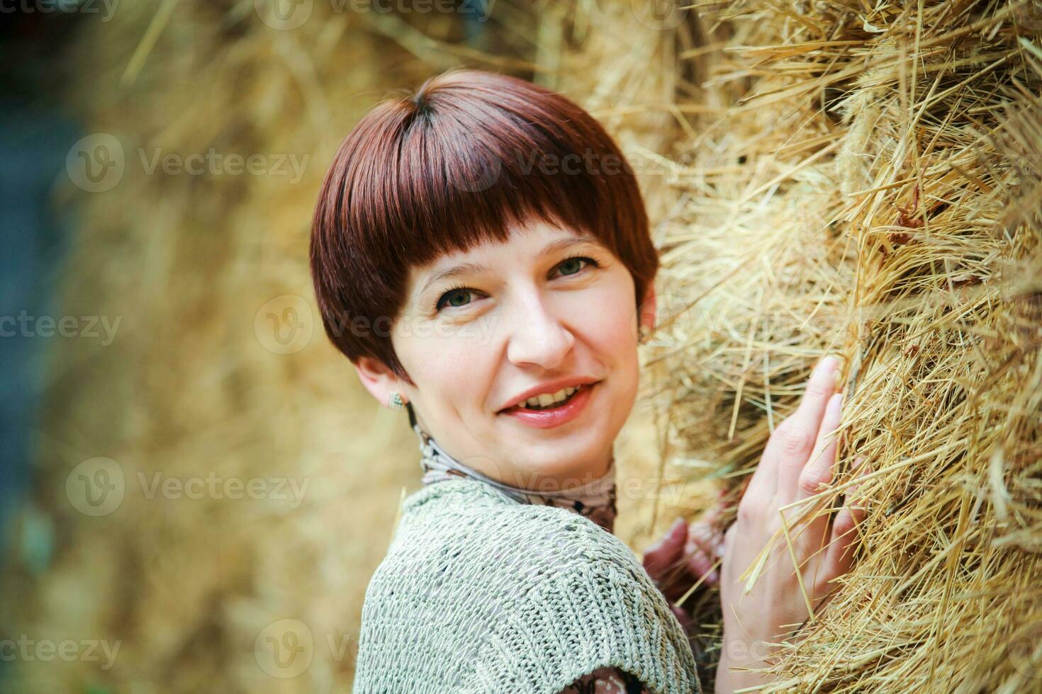 bellissimo donna con corto capelli sembra in il telaio. ritratto di un' trentenne donna. un' ragazza nel un' stabile nel il sfondo di covoni di fieno. foto