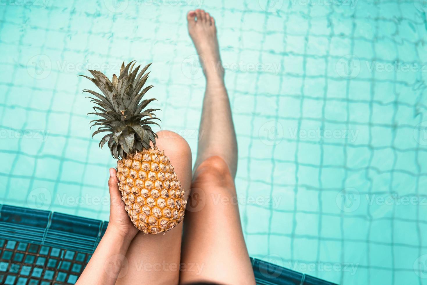 la donna si rilassa in piscina mentre tiene in mano un ananas foto