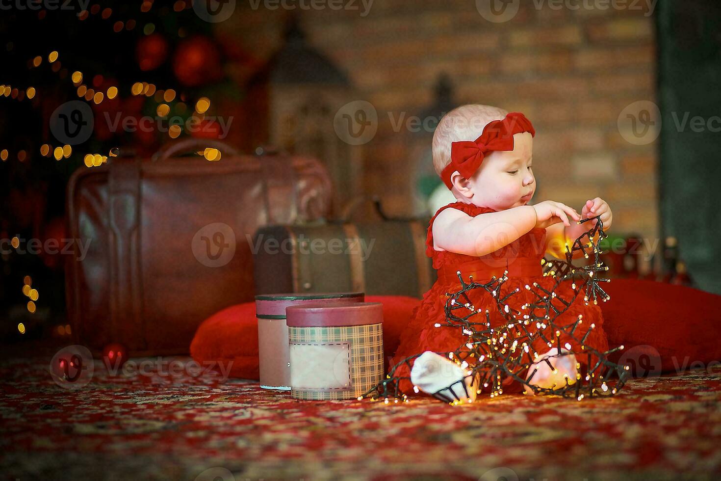 poco ragazza nel rosso vestito contro sfondo di Natale albero detiene Natale ghirlanda nel sua mani. bambino 6 mese vecchio celebra Natale. foto