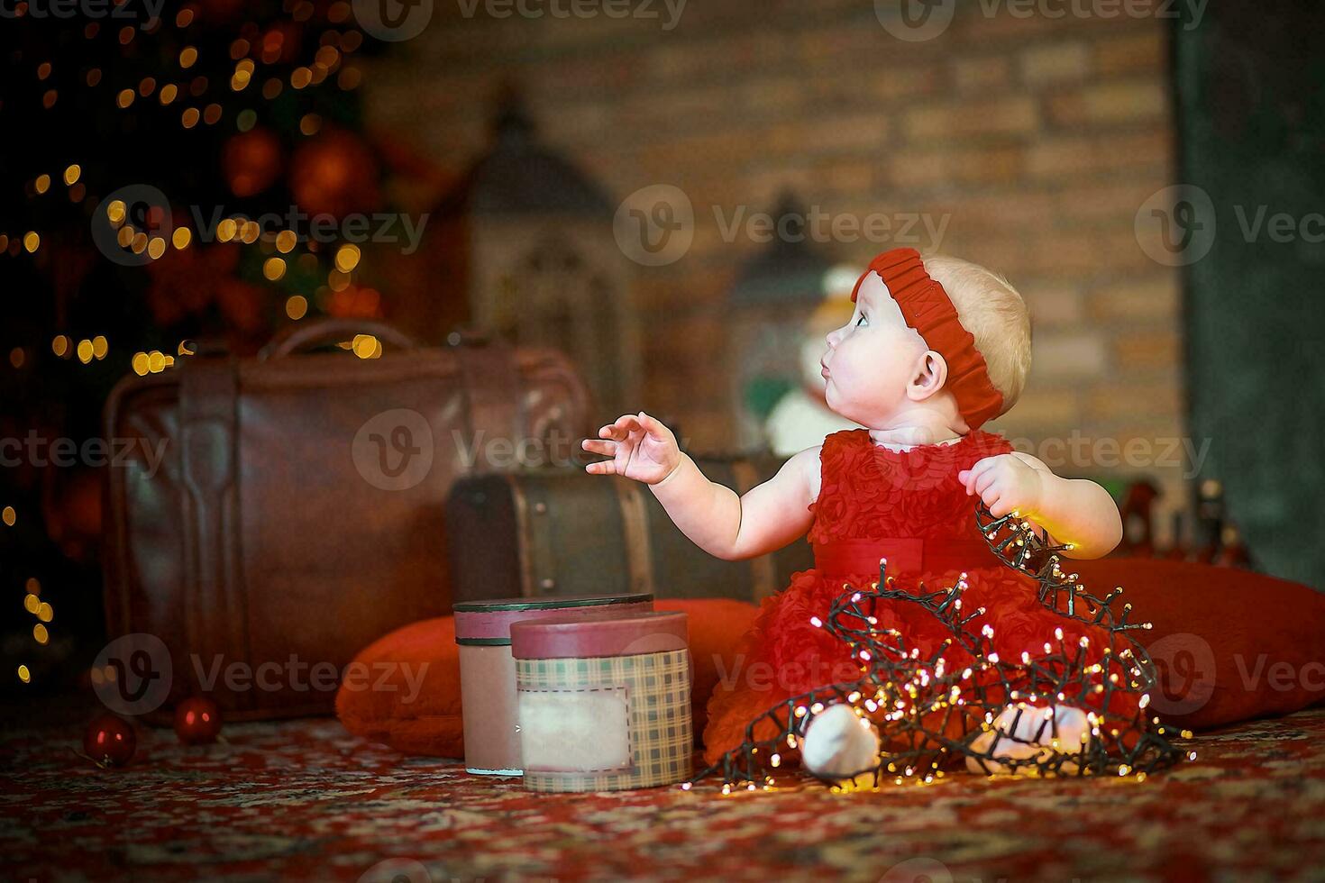 poco ragazza nel rosso vestito contro sfondo di Natale albero detiene Natale ghirlanda nel sua mani. bambino 6 mese vecchio celebra Natale. foto