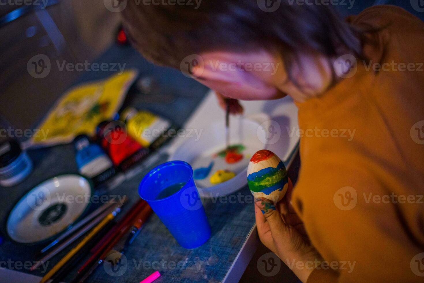 un' bambino decora un Pasqua uovo nel il colori di il arcobaleno. un' bambino detiene un uovo e vernici esso con un' spazzola. preparazione per il celebrazione di Pasqua. foto