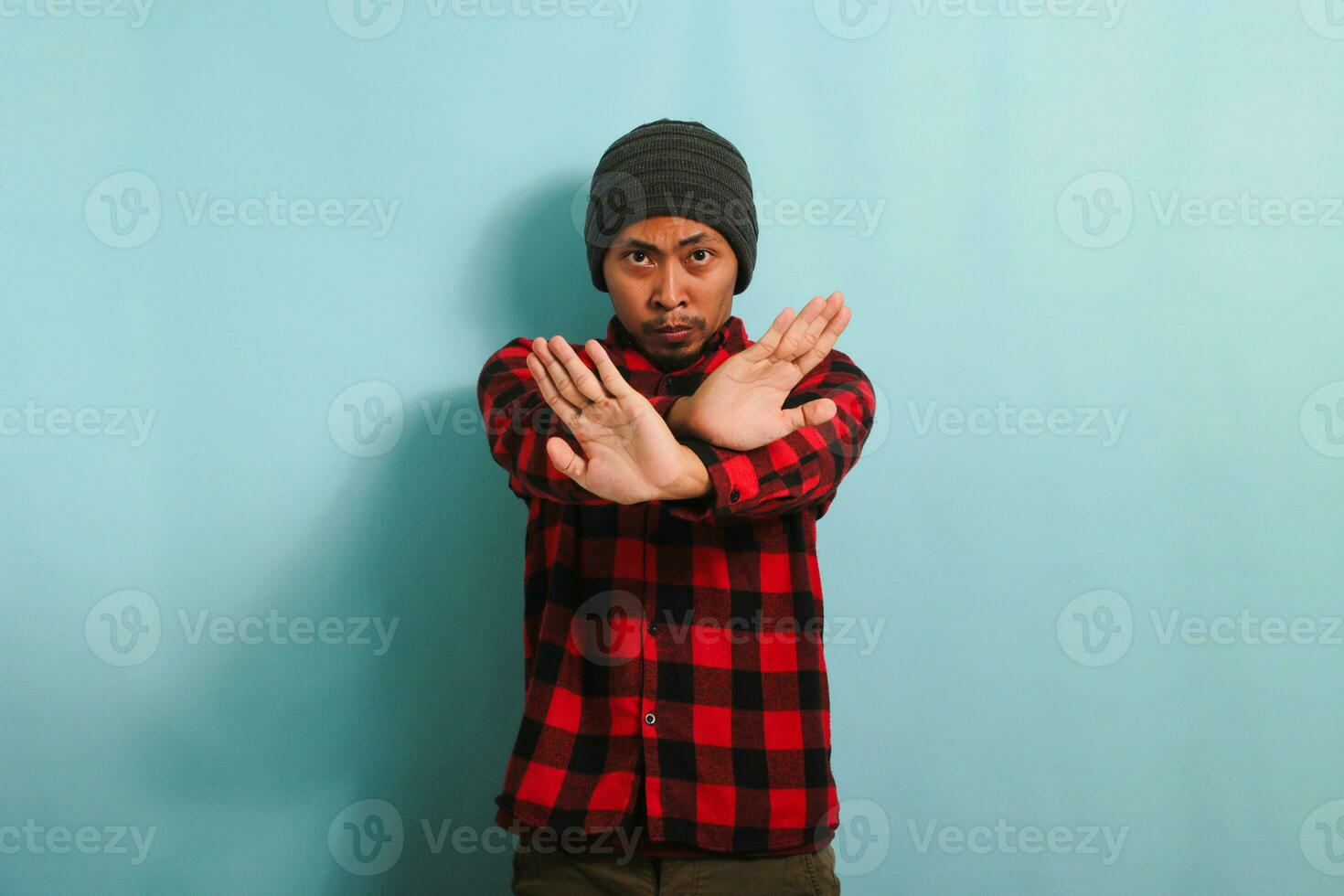 arrabbiato giovane asiatico uomo sta con il suo braccia attraversato, fermare gesto, isolato su blu sfondo. foto