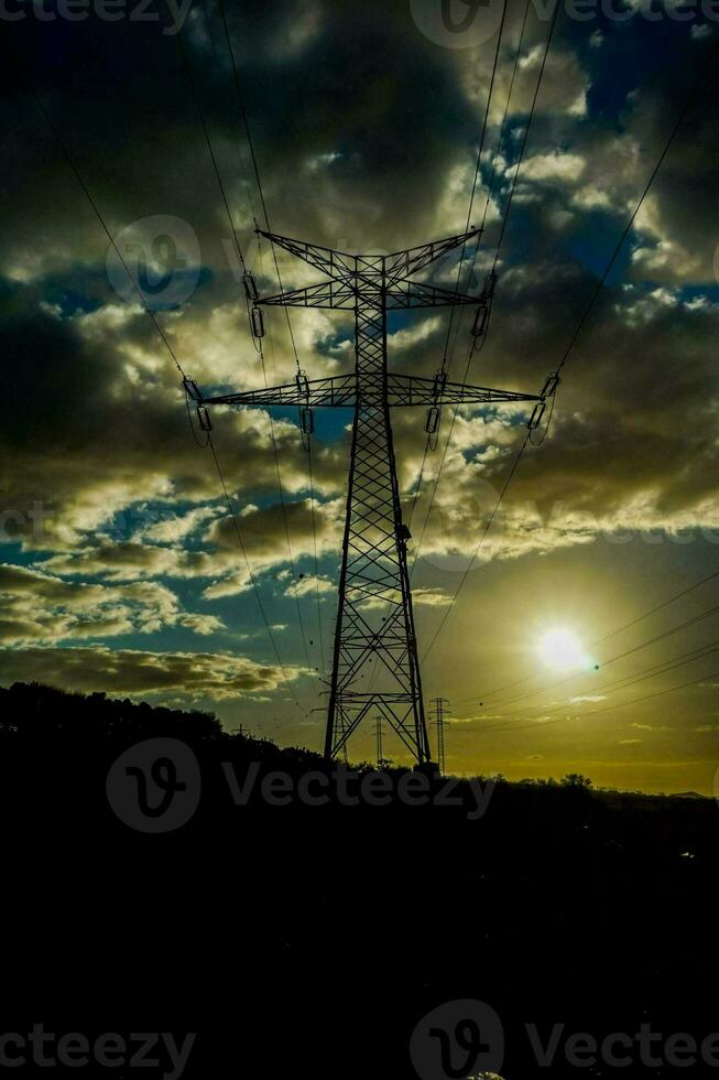 un' silhouette di un elettricità Torre contro un' nuvoloso cielo foto