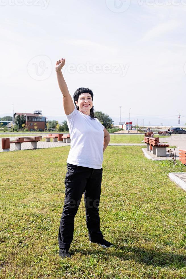donna in abiti sportivi che si esercita nel parco in piedi con le braccia alzate foto