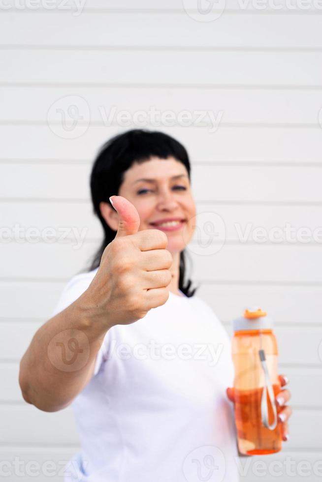 donna che mostra i pollici in su in piedi all'aperto su sfondo grigio solido foto