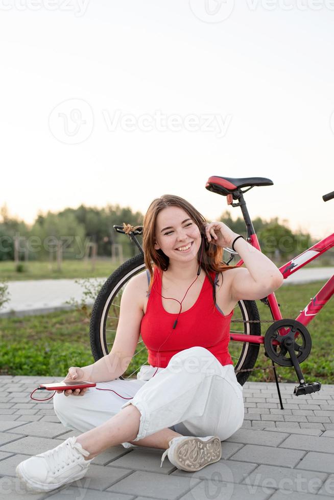 ragazza seduta accanto alla sua bici nel parco ascoltando musica foto