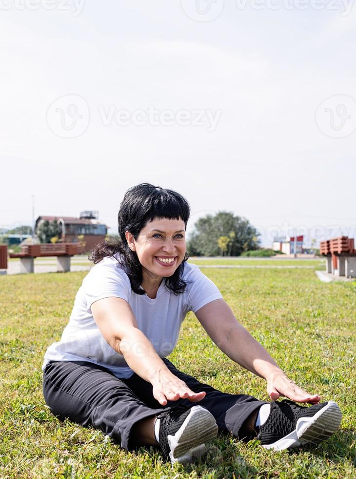 donna in fase di riscaldamento stretching seduta sull'erba nel parco foto