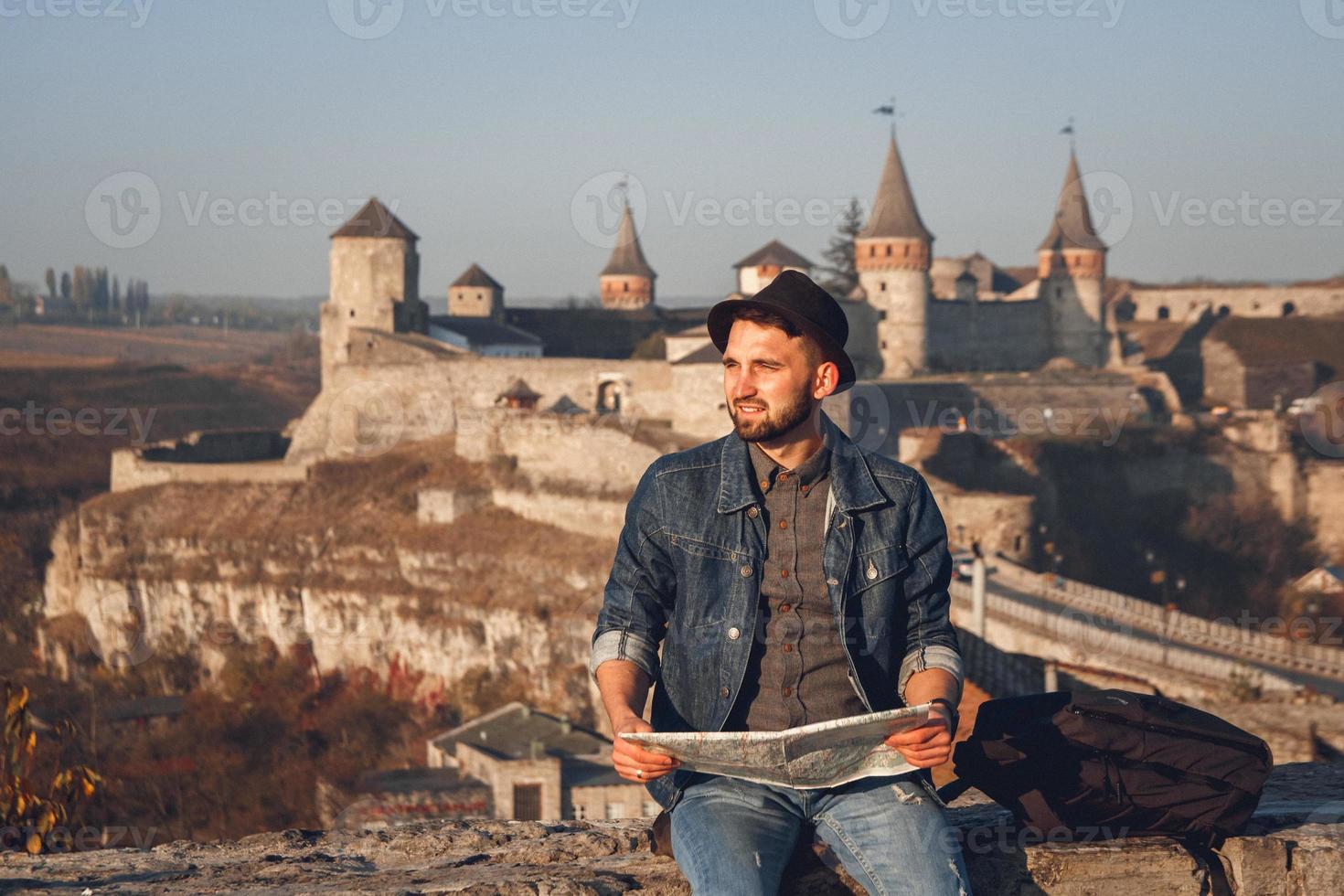 l'uomo viaggiatore con una mappa in mano si siede sullo sfondo del vecchio castello foto