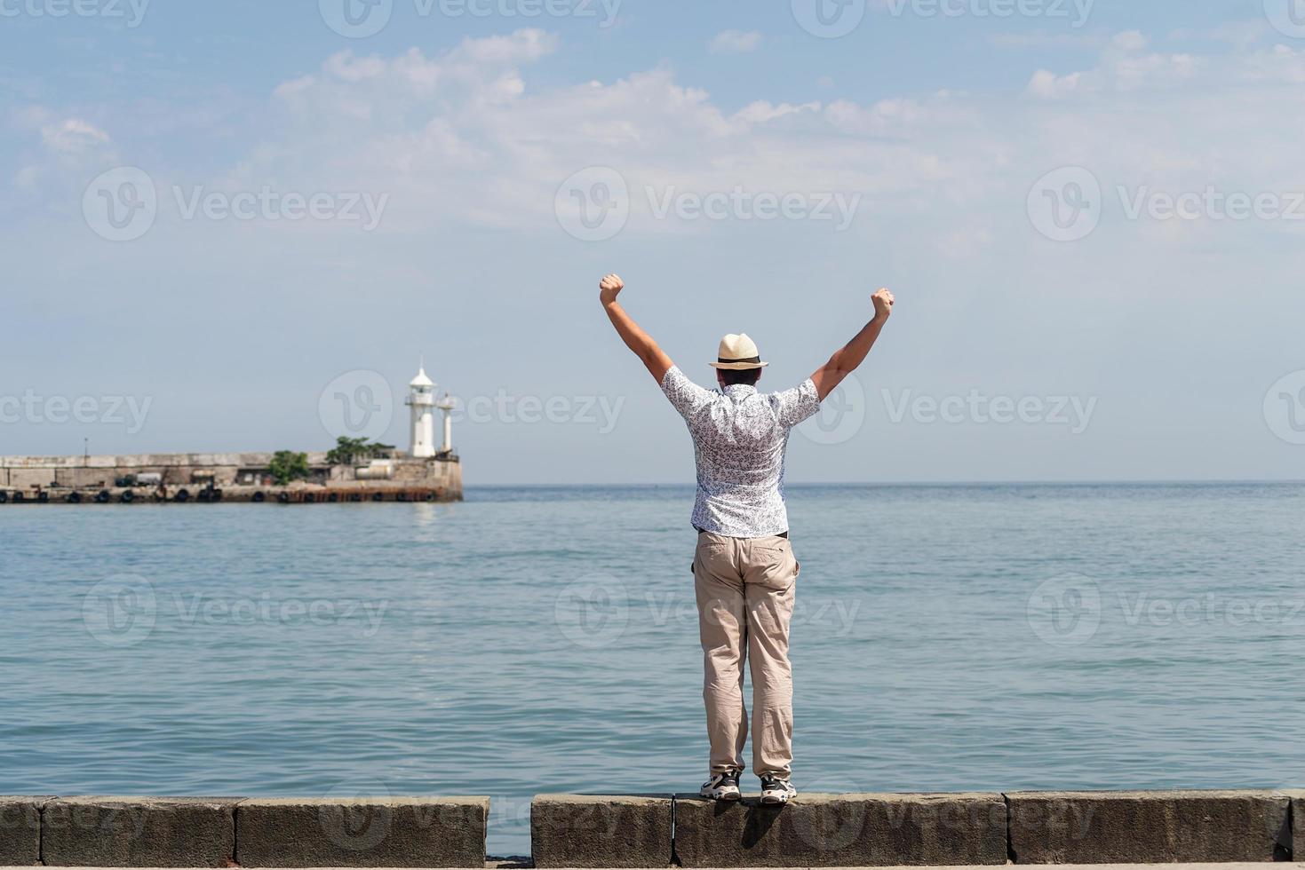 uomo in piedi sul molo con mare e faro sullo sfondo foto