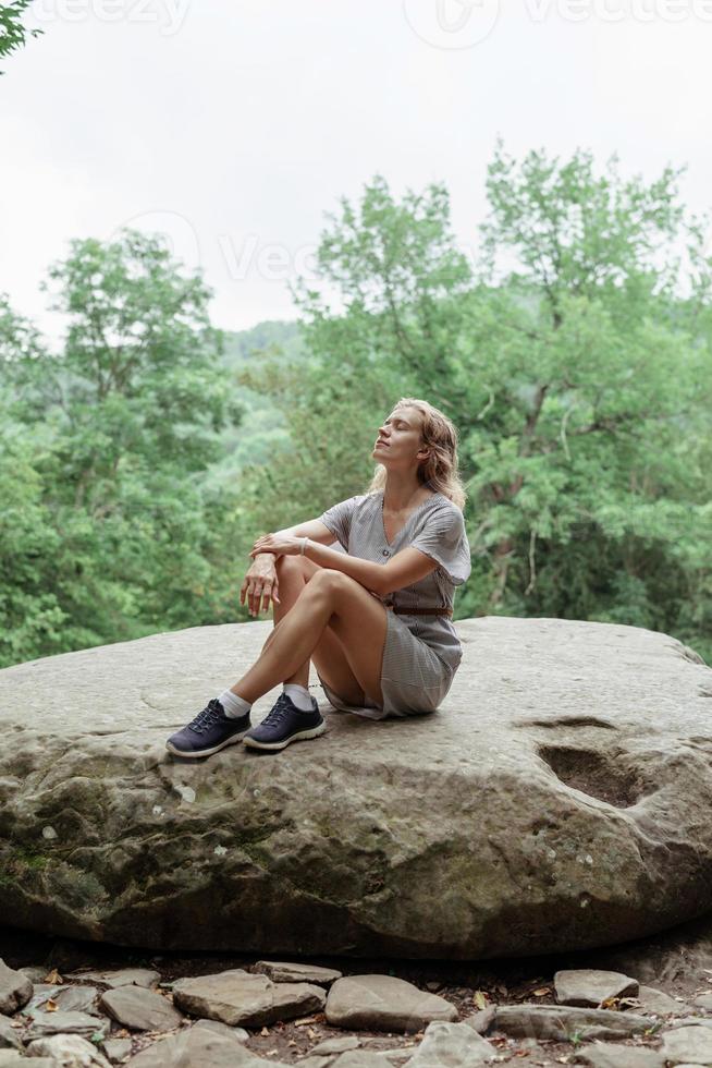 donna seduta su una grande roccia nella foresta, che riposa o medita foto