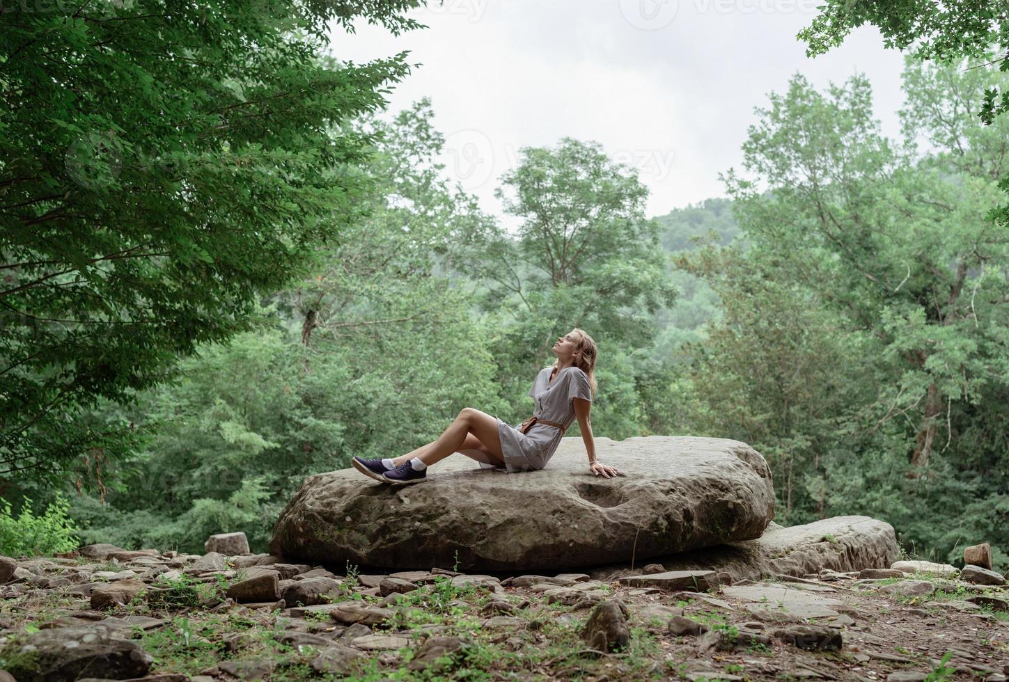 donna seduta su una grande roccia nella foresta, che riposa o medita foto