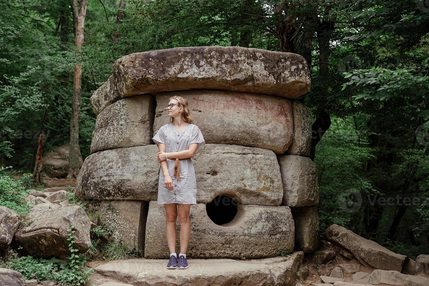 giovane donna che cammina vicino alla grande pietra del dolmen nella foresta foto