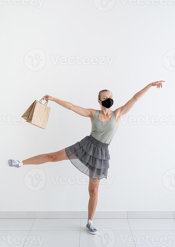 giovane donna che balla balletto con borse della spesa in una maschera protettiva foto