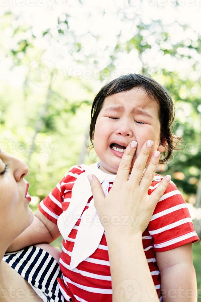 bambina asiatica che piange nelle mani della madre foto