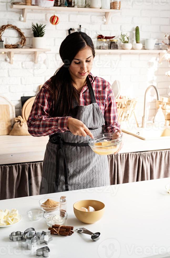 giovane donna latina che sbatte le uova cucinando in cucina foto