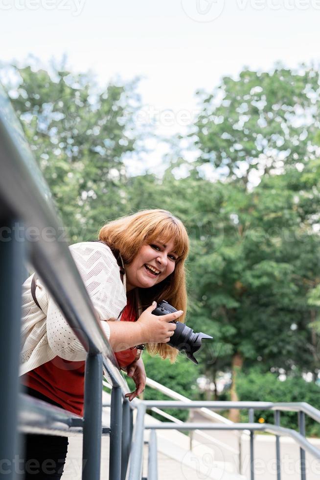 fotografo donna taglie forti all'aperto con in mano una macchina fotografica e ridendo foto
