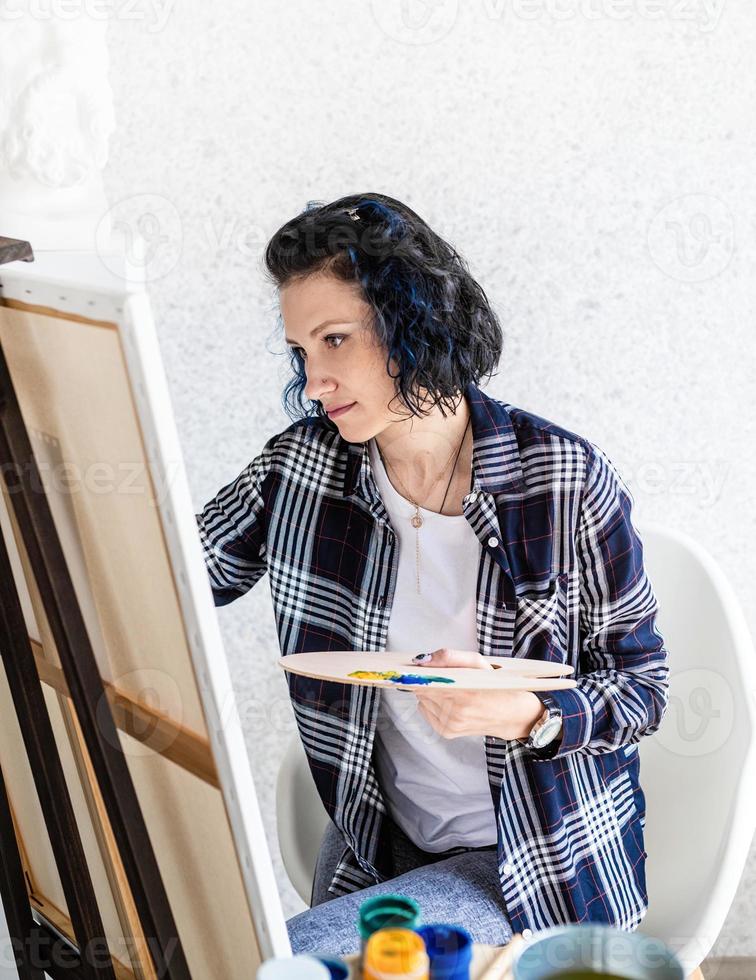 donna creativa con i capelli tinti di blu che dipingono nel suo studio foto