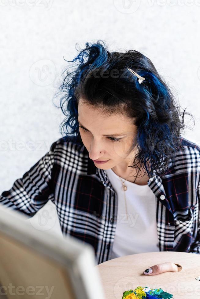 donna creativa con i capelli tinti di blu che dipingono nel suo studio foto