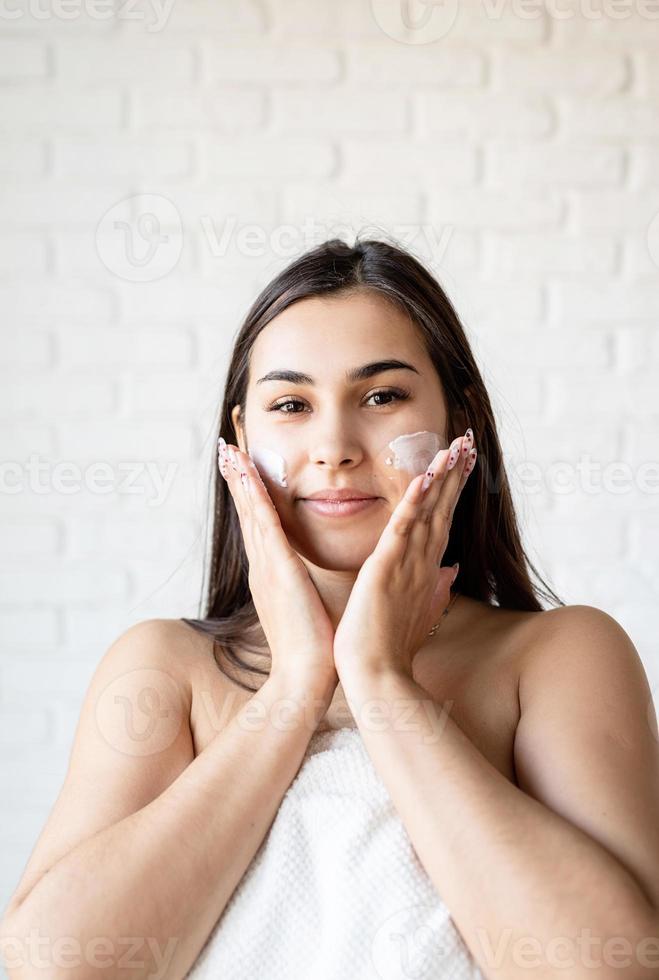 donna che indossa accappatoio applicando la crema per il viso sul viso foto