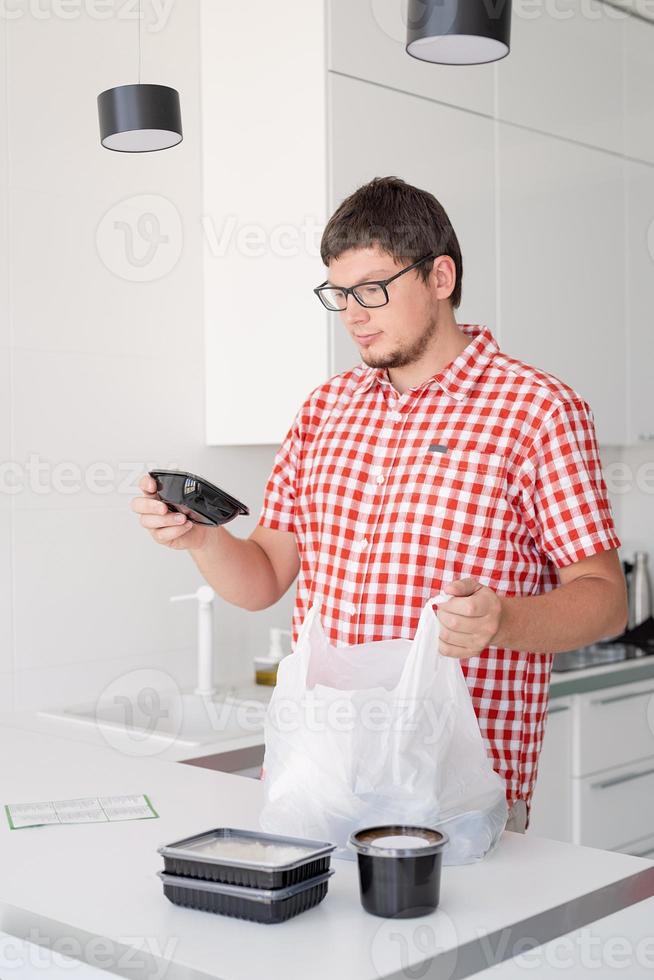 uomo che tiene un sacchetto di plastica usa e getta con consegna di cibo in cucina foto