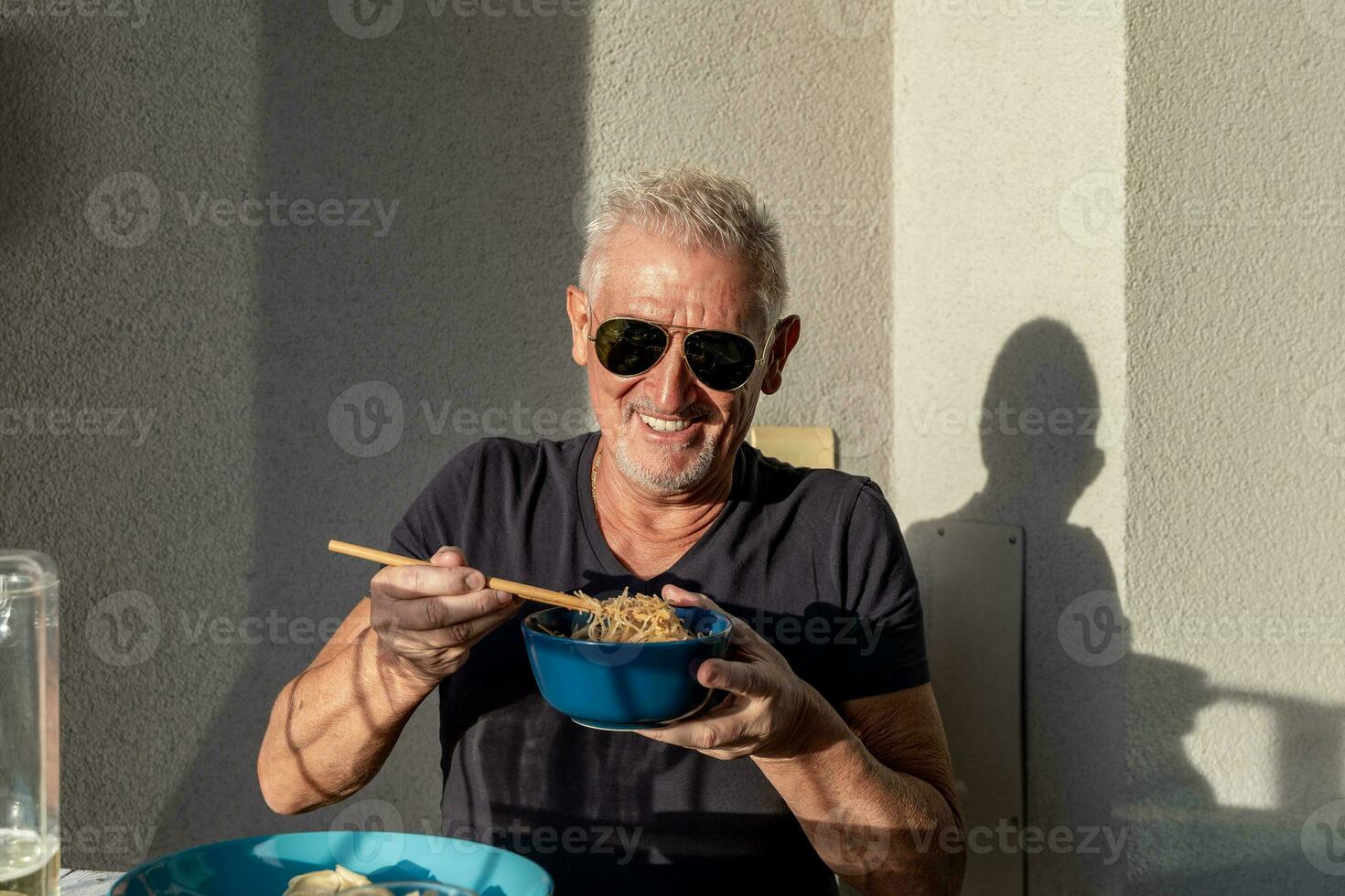 attraente di mezza età uomo avere divertimento mentre mangiare seduta a un' tavolo di cui Cinese prendere lontano cibo foto
