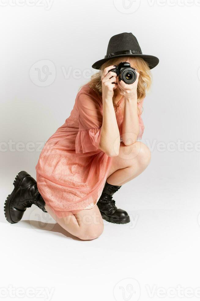ritratto di un' carino ragazza fotografo nel un' cappello in posa con un' telecamera nel sua mani nel il studio su un' bianca sfondo foto