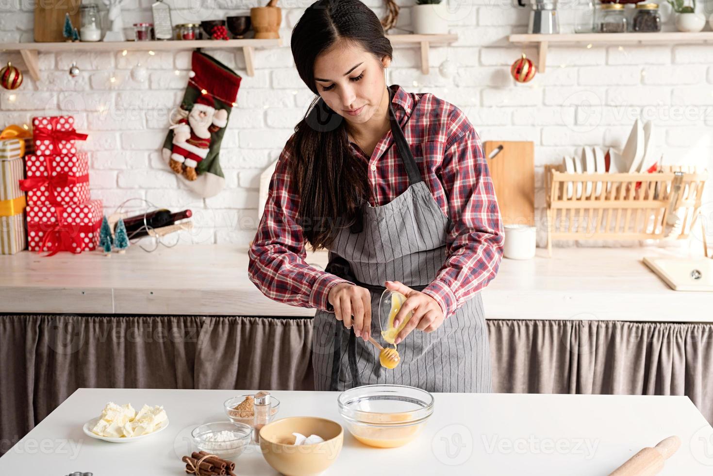 donna latina che versa il miele sull'impasto cucinando in cucina foto