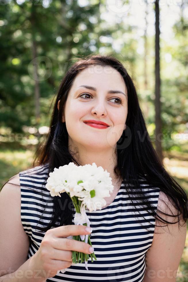 donna bruna adulta di mezza età in piedi all'aperto annusando fiori freschi foto